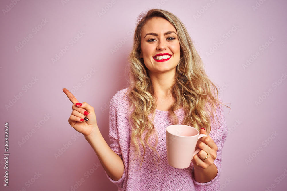 Young beautiful woman wearing sweater drinking a cup of coffee over pink isolated background very happy pointing with hand and finger to the side Young beautiful woman wearing sweater drinking a cup of coffee over pink isolated background very happy pointing with hand and finger to the side