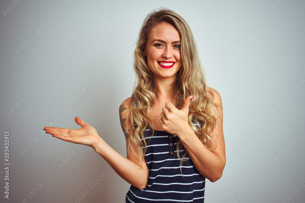 Young beautiful woman wearing stripes t-shirt standing over white isolated background Showing palm hand and doing ok gesture with thumbs up, smiling happy and cheerful