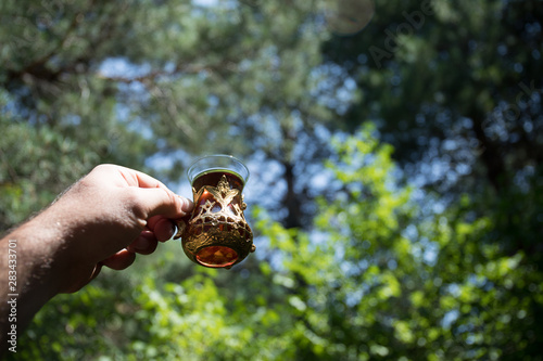 Eastern black tea in glass at the forest. Eastern tea concept. Armudu traditional cup. Green nature background.