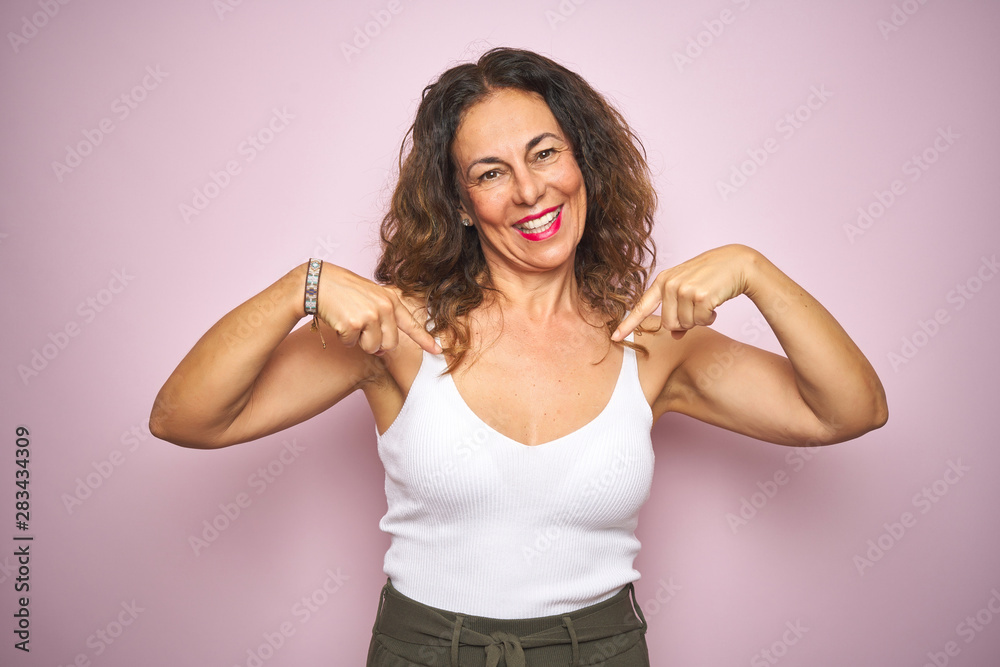 Middle age senior woman standing over pink isolated background looking confident with smile on face, pointing oneself with fingers proud and happy.
