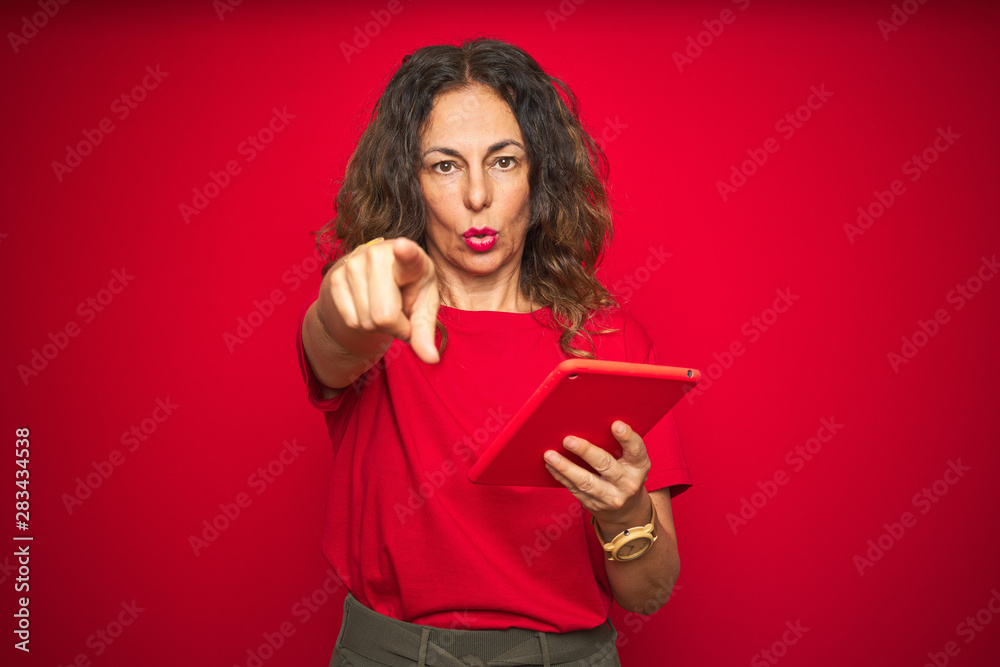 Middle age senior woman using touchpad tablet over red isolated background pointing with finger to the camera and to you, hand sign, positive and confident gesture from the front