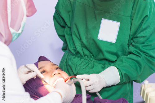close up of muslim hijab female removing tartar or calculus scaling from teeth with dentist and assistant