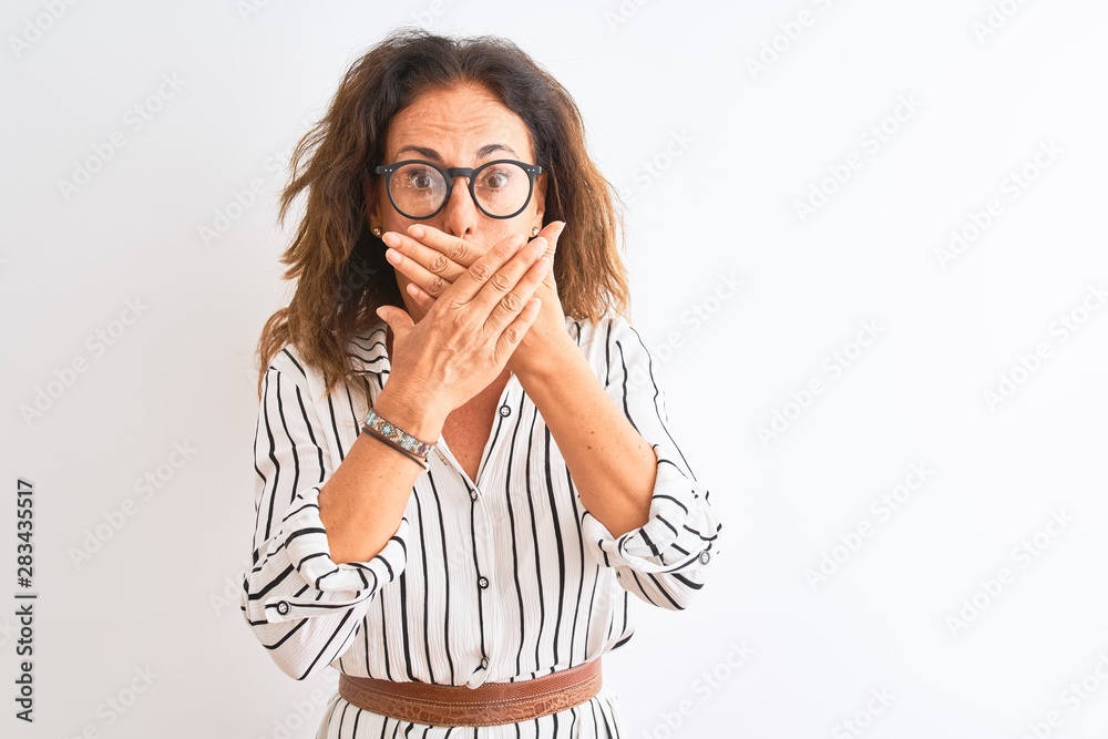 Middle age businesswoman wearing striped dress and glasses over isolated white background shocked covering mouth with hands for mistake. Secret concept. Middle age businesswoman wearing striped dress and glasses over isolated white background shocked covering mouth with hands for mistake. Secret concept.