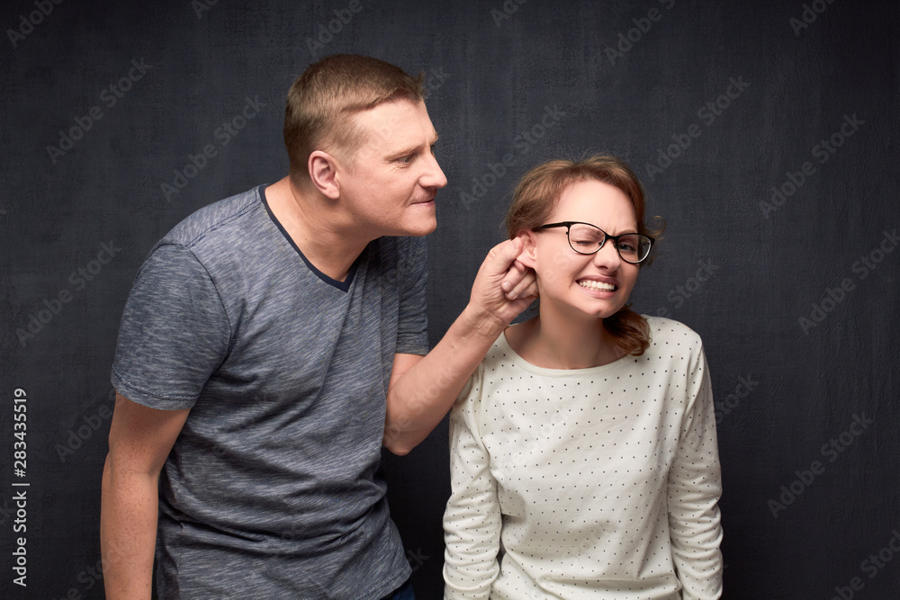 Dissatisfied man is pulling woman by ear while scolding Stock Photo