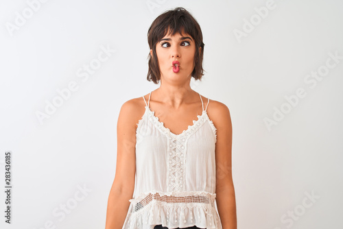 Young beautiful woman wearing summer casual t-shirt standing over isolated white background making fish face with lips, crazy and comical gesture. Funny expression.