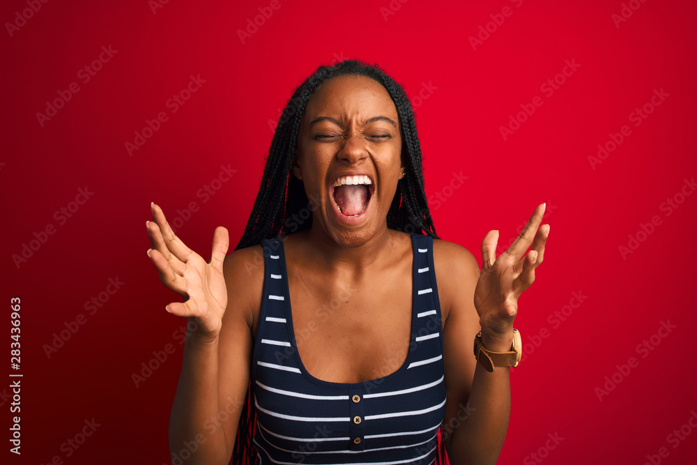 Young african american woman wearing striped t-shirt standing over isolated red background celebrating mad and crazy for success with arms raised and closed eyes screaming excited. Winner concept Young african american woman wearing striped t-shirt standing over isolated red background celebrating mad and crazy for success with arms raised and closed eyes screaming excited. Winner concept