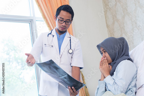 Portrait of Asian male doctor with his female patient in the hospital clinic explaining xray results photo