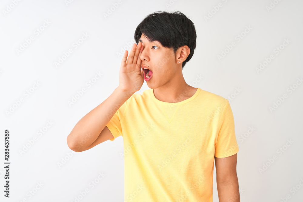 Chinese man wearing yellow casual t-shirt standing over isolated white background shouting and screaming loud to side with hand on mouth. Communication concept. Chinese man wearing yellow casual t-shirt standing over isolated white background shouting and screaming loud to side with hand on mouth. Communication concept.