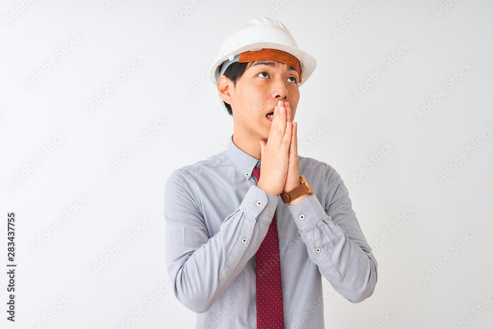 Chinese architect man wearing tie and helmet standing over isolated white background begging and praying with hands together with hope expression on face very emotional and worried. 