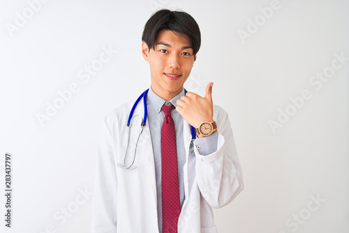 Chinese doctor man wearing coat tie and stethoscope over isolated white background doing happy thumbs up gesture with hand. Approving expression looking at the camera with showing success.