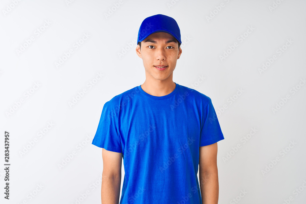 Chinese deliveryman wearing blue t-shirt and cap standing over isolated white background with a happy and cool smile on face. Lucky person. Chinese deliveryman wearing blue t-shirt and cap standing over isolated white background with a happy and cool smile on face. Lucky person.
