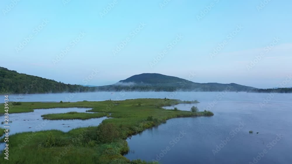 Wide aerial sunrise shot over grass and water under mountain peak. Wide aerial sunrise shot over grass and water under mountain peak.