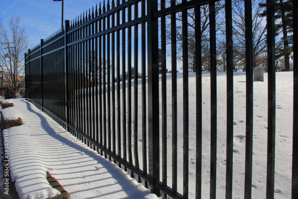Snow covered ledge, framed by a black rod iron fence, and blue sky.