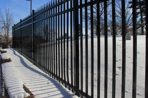 Snow covered ledge, framed by a black rod iron fence, and blue sky.