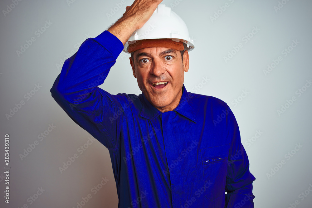 Handsome middle age worker man wearing uniform and helmet over isolated white background surprised with hand on head for mistake, remember error. Forgot, bad memory concept.