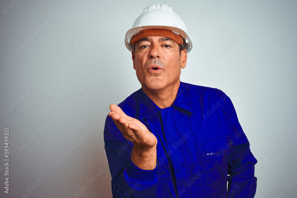 Handsome middle age worker man wearing uniform and helmet over isolated white background looking at the camera blowing a kiss with hand on air being lovely and sexy. Love expression. Handsome middle age worker man wearing uniform and helmet over isolated white background looking at the camera blowing a kiss with hand on air being lovely and sexy. Love expression.