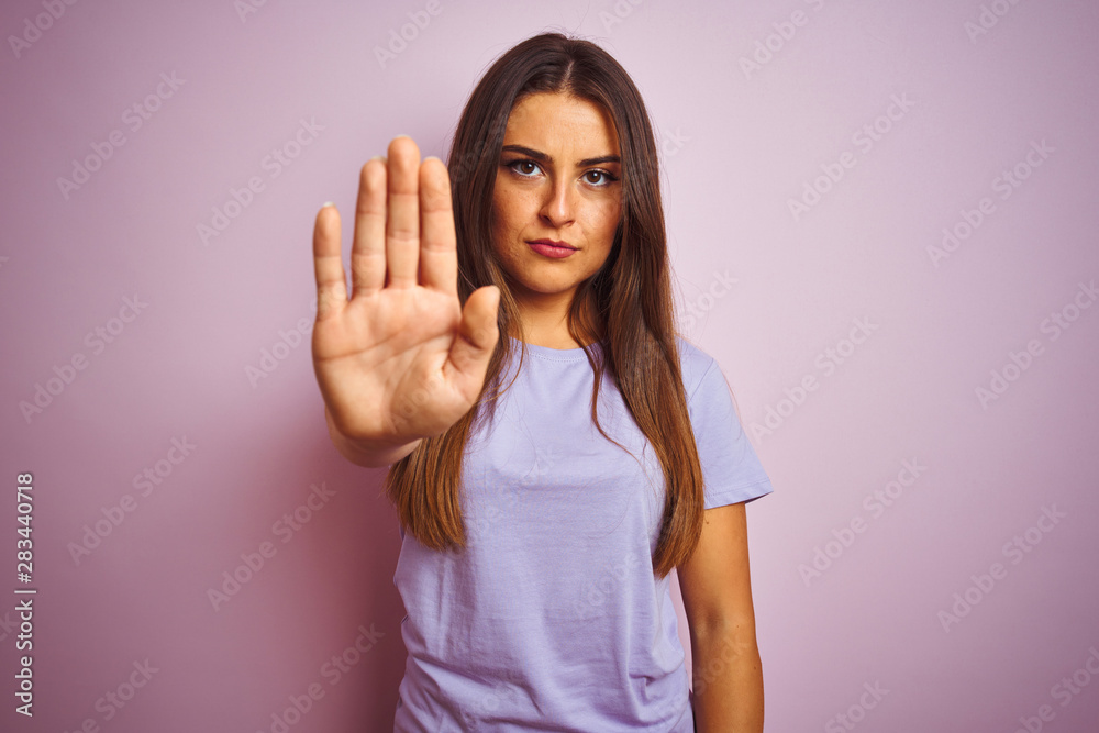 Young beautiful woman wearing casual t-shirt standing over isolated pink background doing stop sing with palm of the hand. Warning expression with negative and serious gesture on the face. Young beautiful woman wearing casual t-shirt standing over isolated pink background doing stop sing with palm of the hand. Warning expression with negative and serious gesture on the face.