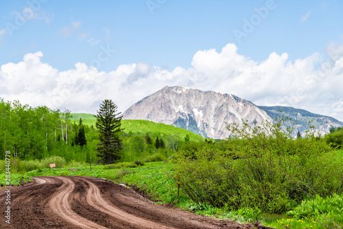 Crested Butte Kebler Pass rocky mountain view and dirt unpaved road with clouds in sky in green summer