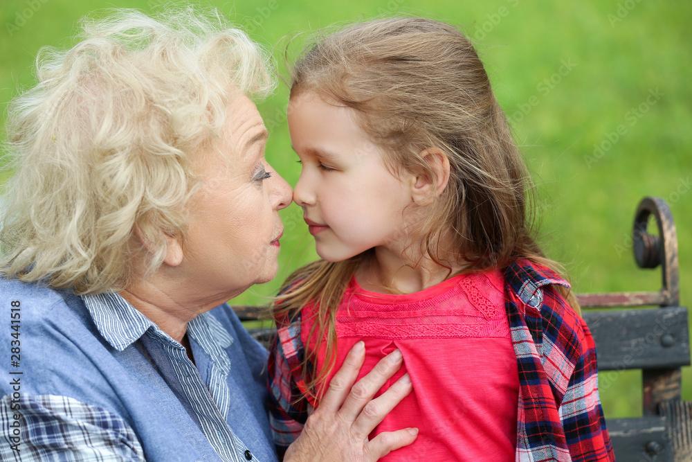 Cute little girl with grandmother sitting on bench in park
