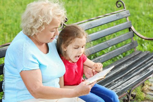 Cute little girl reading book with grandmother in park