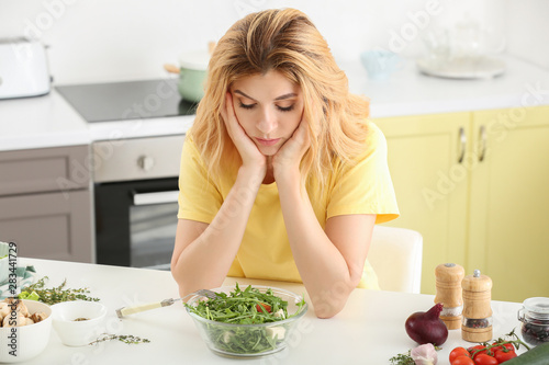 Reluctant woman with healthy vegetable salad in kitchen