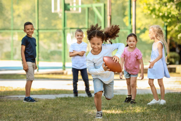 Cute little children playing with rugby ball in park