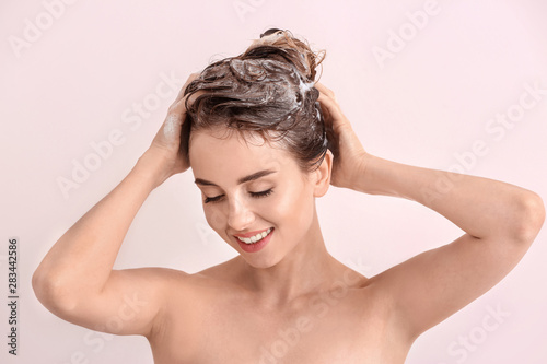 Beautiful young woman washing hair against light color background