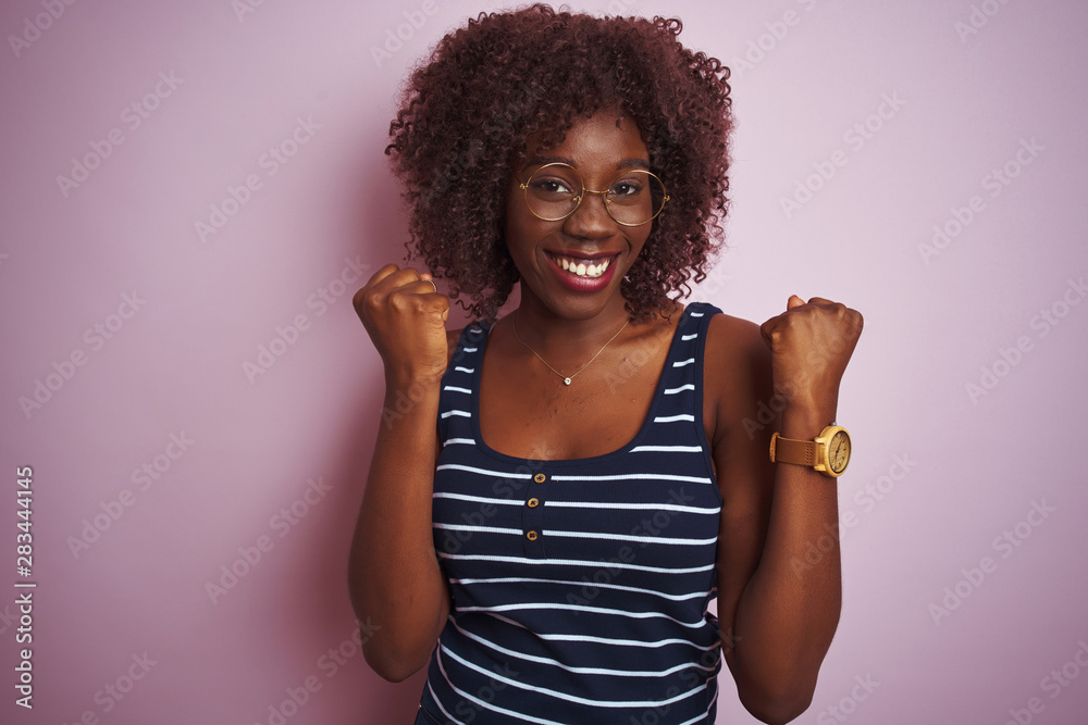 Young african afro woman wearing striped t-shirt glasses over isolated pink background celebrating surprised and amazed for success with arms raised and open eyes. Winner concept.