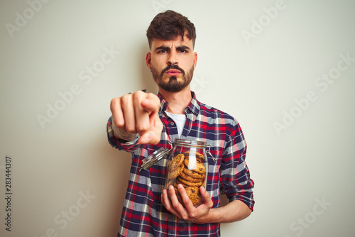 Young man wearing bathrobe drinking cup of coffee standing over isolated white background pointing with finger to the camera and to you, hand sign, positive and confident gesture from the front