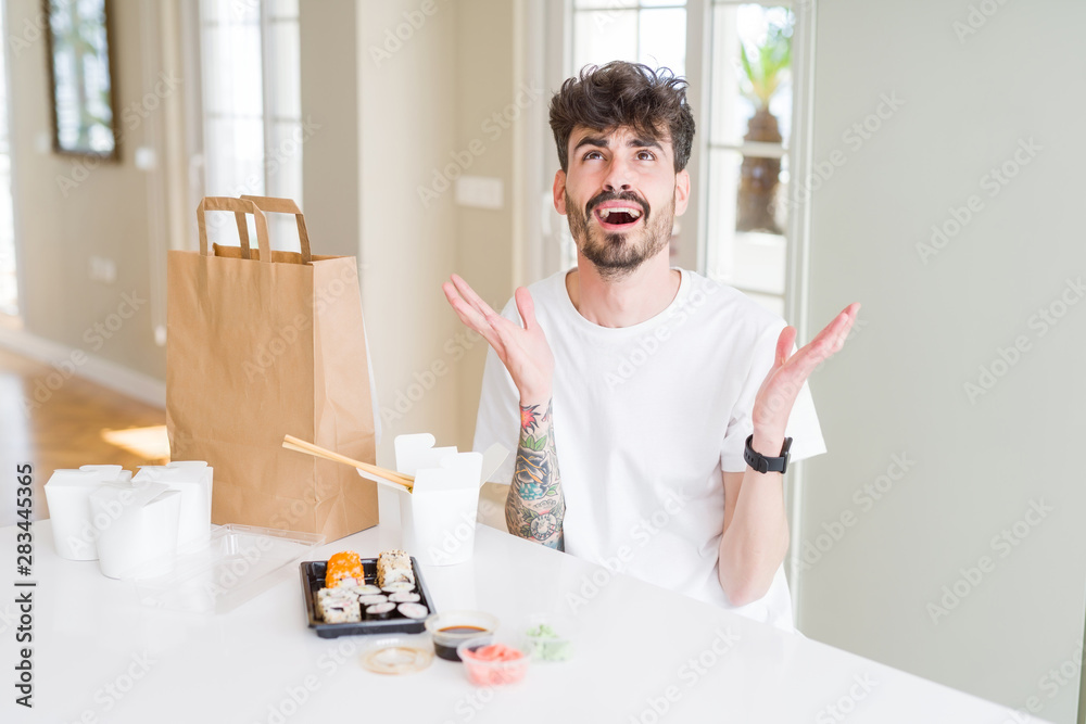 Young man eating asian sushi from home delivery crazy and mad shouting and yelling with aggressive expression and arms raised. Frustration concept.