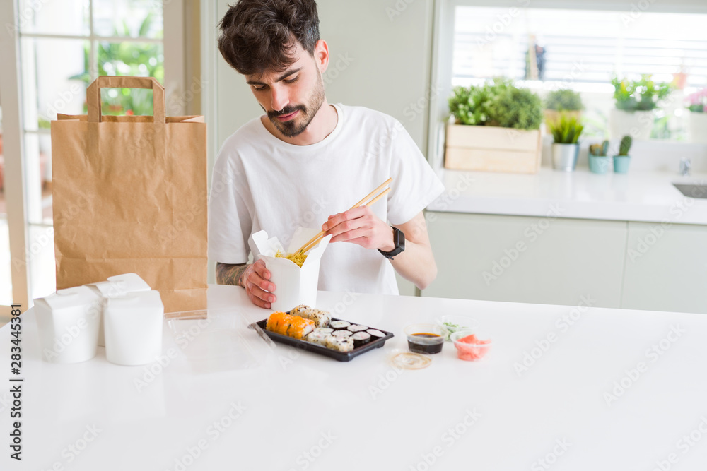 Young man eating sushi asian food and noodles using choopsticks from take away delivery