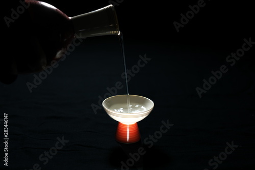 Tokyo,Japan-August 12, 2019: Pouring sake or Nihonshu or Japanese rice wine into a sake cup or Ochoko from a sake bot or tokkuri