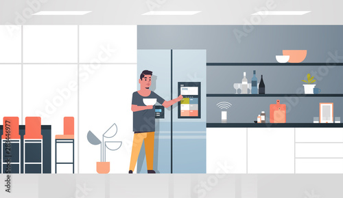 man touching refrigerator screen with smart speaker voice recognition activated digital assistant concept modern kitchen interior flat horizontal full length