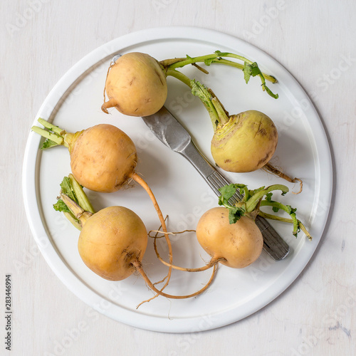 Ripe yellow turnip on a white round dish on a light wooden background. Selective focus.