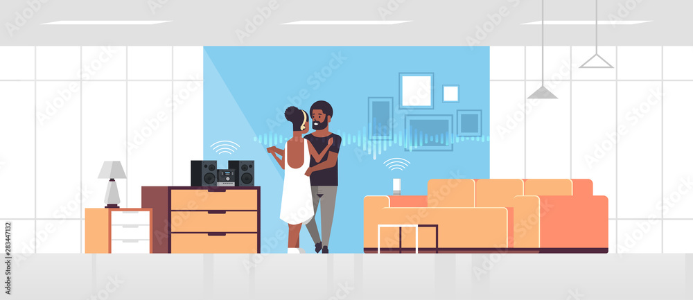 couple using Hi-Fi stereo system controlled by smart speaker voice recognition activated assistant smart home concept african american man woman dancing living room interior full length horizontal
