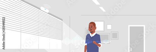 african american man using smart speaker voice recognition activated digital assistant concept modern living room interior flat horizontal portrait