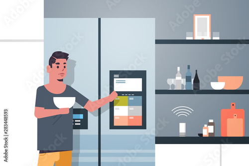man touching refrigerator screen with smart speaker voice recognition activated digital assistant concept modern kitchen interior flat horizontal portrait