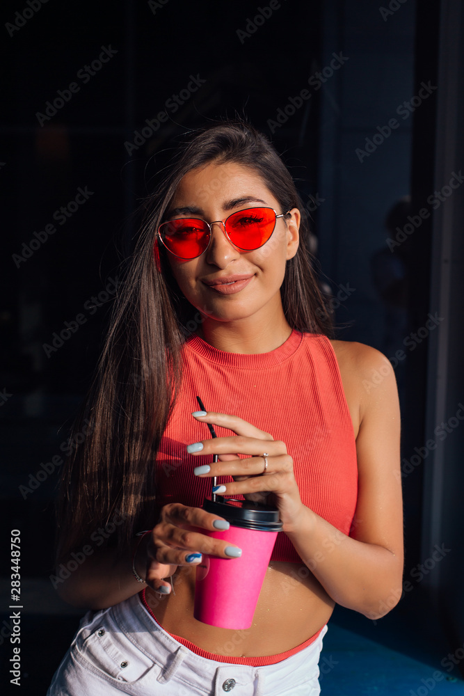 Obraz premium Stylish happy young brunette woman holding pink cup of coffee to go.
