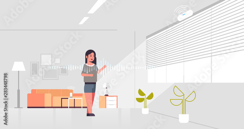 casual woman using smart speaker voice recognition activated digital assistant concept modern living room interior flat horizontal full length
