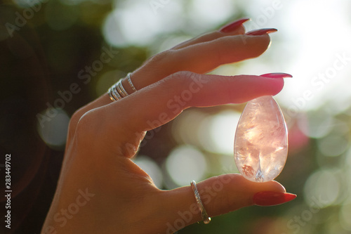 Female hand with transparent amethyst quartz yoni egg for vumfit, imbuilding or meditation. Shining crystal egg in hands on sunrise background outdoors. Womens healthand unity with the nature concept photo