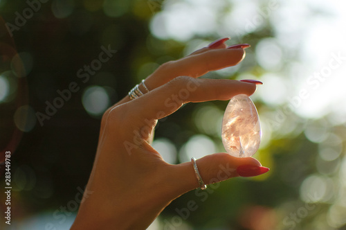 Female hand with transparent amethyst quartz yoni egg for vumfit, imbuilding or meditation. Shining crystal egg in hands on sunrise background outdoors. Womens healthand unity with the nature concept photo