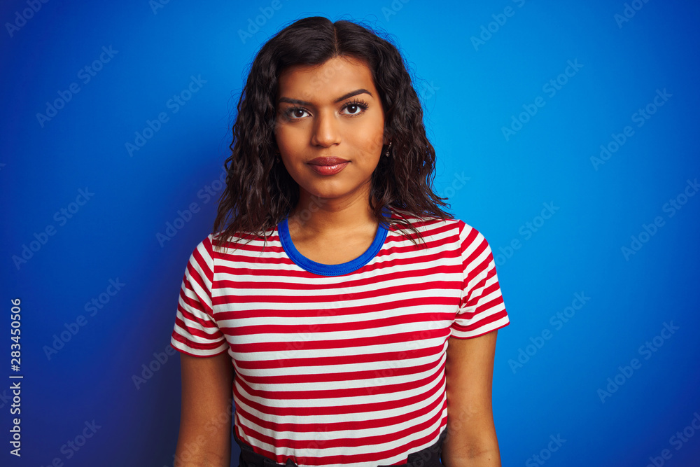 Transsexual transgender woman wearing stiped t-shirt over isolated blue background with serious expression on face. Simple and natural looking at the camera. Transsexual transgender woman wearing stiped t-shirt over isolated blue background with serious expression on face. Simple and natural looking at the camera.