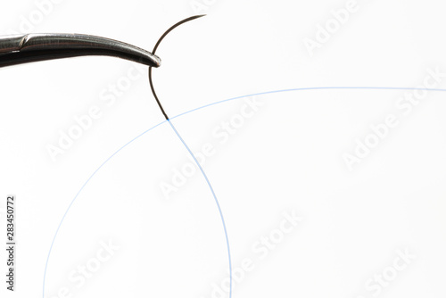 Needle holder with curved needle with blue thread.