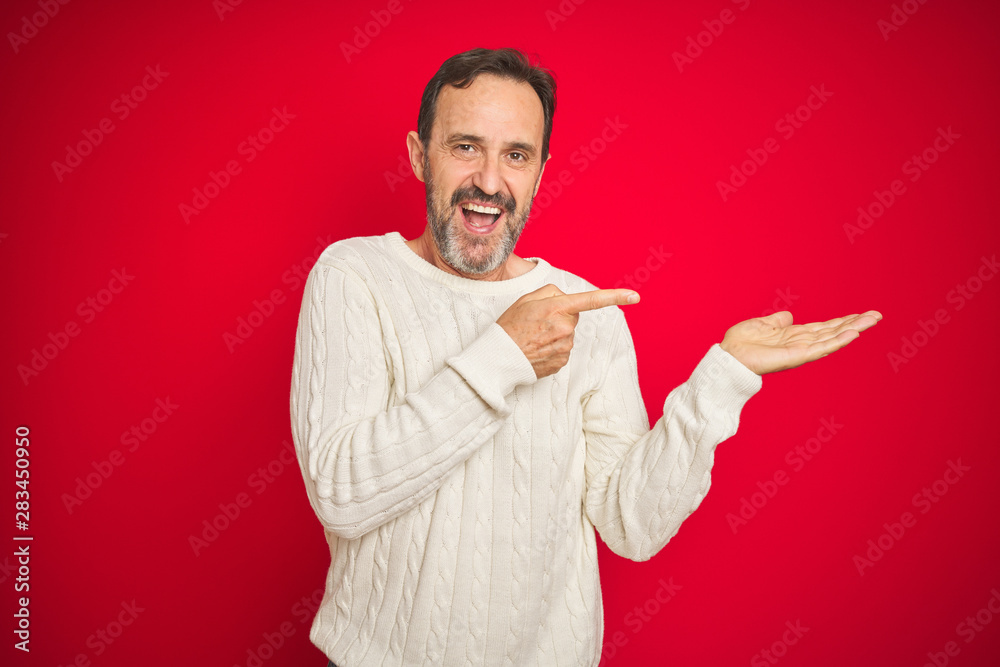 Fototapeta premium Handsome middle age senior man with grey hair over isolated red background amazed and smiling to the camera while presenting with hand and pointing with finger.