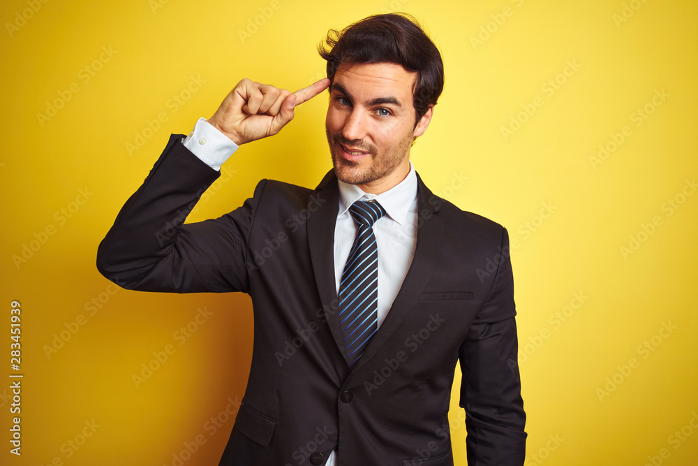 Young handsome businessman wearing suit and tie standing over isolated yellow background Smiling pointing to head with one finger, great idea or thought, good memory Young handsome businessman wearing suit and tie standing over isolated yellow background Smiling pointing to head with one finger, great idea or thought, good memory