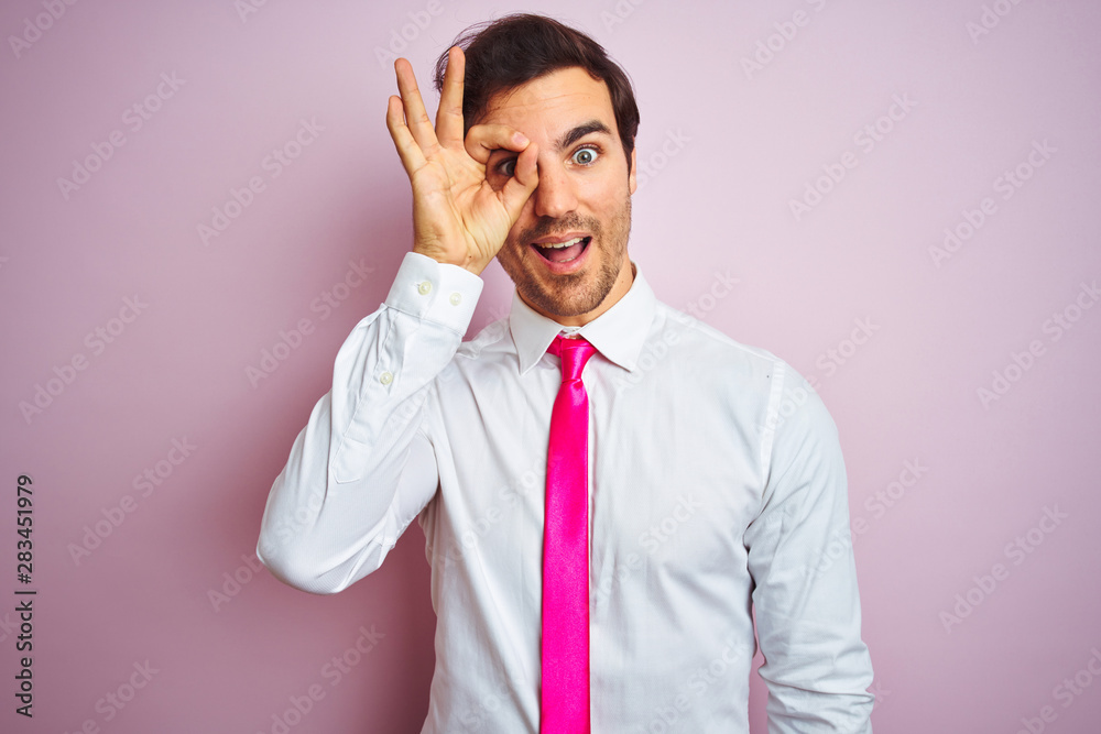Young handsome businessman wearing shirt and tie standing over isolated pink background doing ok gesture with hand smiling, eye looking through fingers with happy face. Young handsome businessman wearing shirt and tie standing over isolated pink background doing ok gesture with hand smiling, eye looking through fingers with happy face.