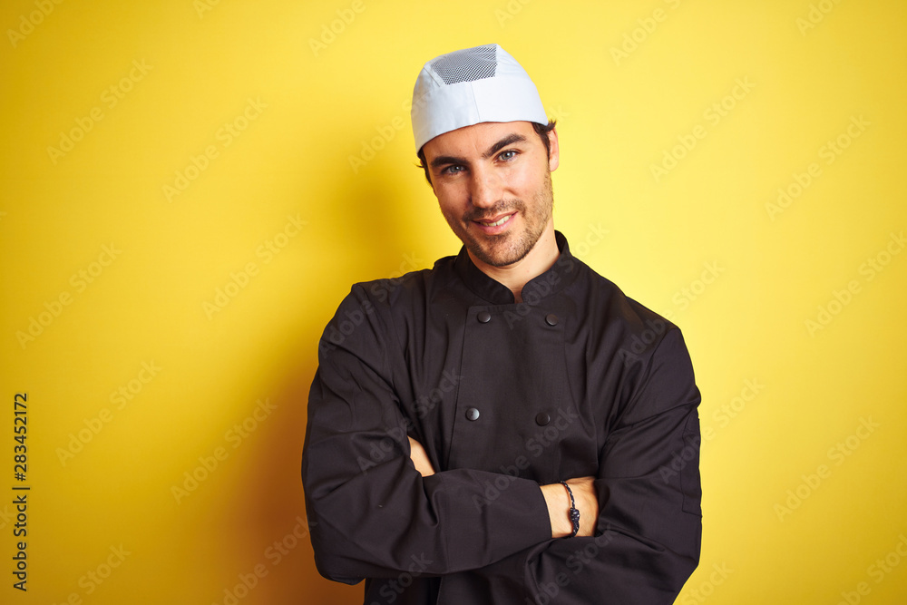 Young handsome chef man cooking wearing uniform and hat over isolated yellow background happy face smiling with crossed arms looking at the camera. Positive person. Young handsome chef man cooking wearing uniform and hat over isolated yellow background happy face smiling with crossed arms looking at the camera. Positive person.