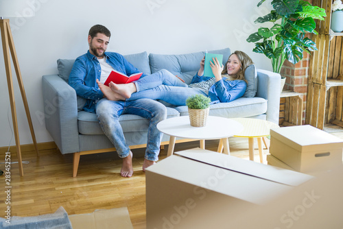 Young couple relaxing on the sofa reading a book, taking a break for moving to new house