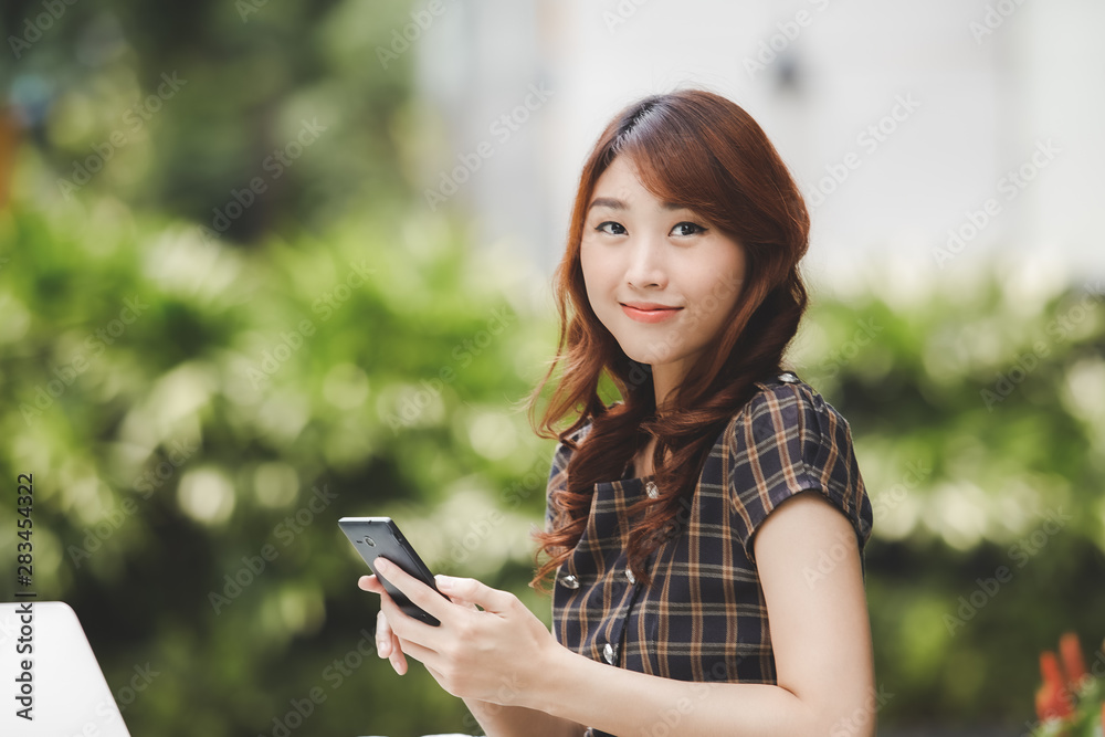 Beautiful asian girl holding smartphone with laptop on the table Beautiful asian girl holding smartphone with laptop on the table