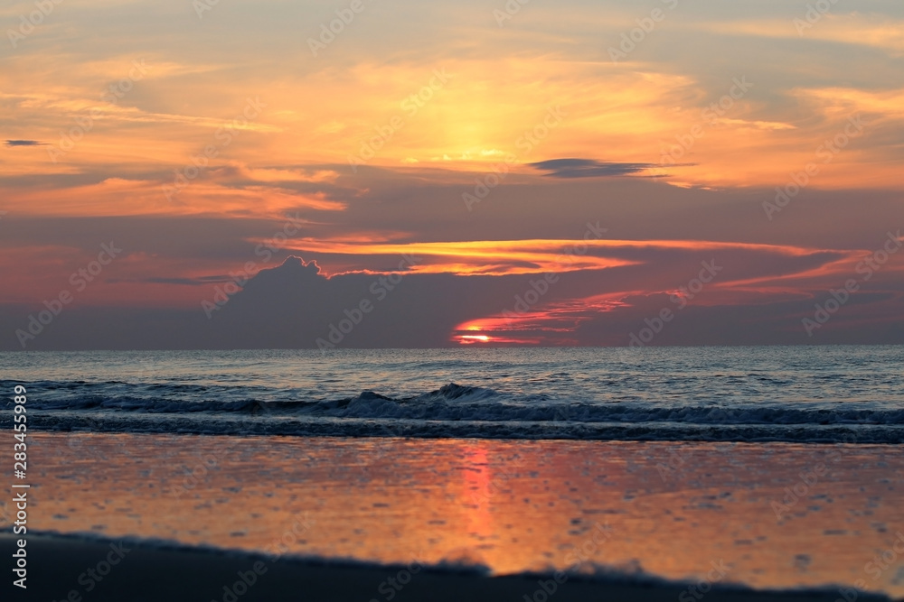 Landscape with dramatic sunrise over the Atlantic ocean in South Carolina, USA, Myrtle Beach area. Front view of calm ocean rippling waves and sunlight reflection in low tide.